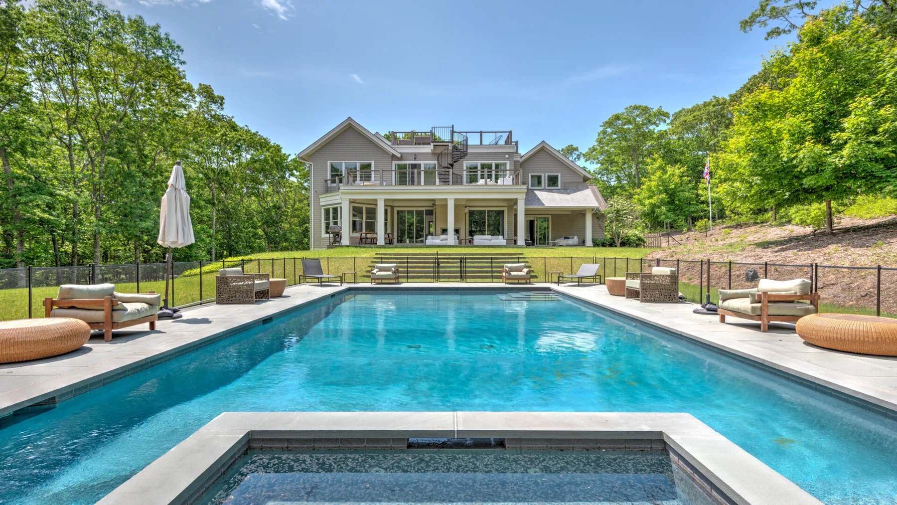 Outdoor swimming pool with lounge seating in front of a large house.
