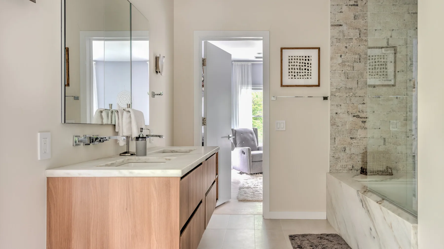 Un baño luminoso con un tocador de madera, lavabo y ducha de vidrio.