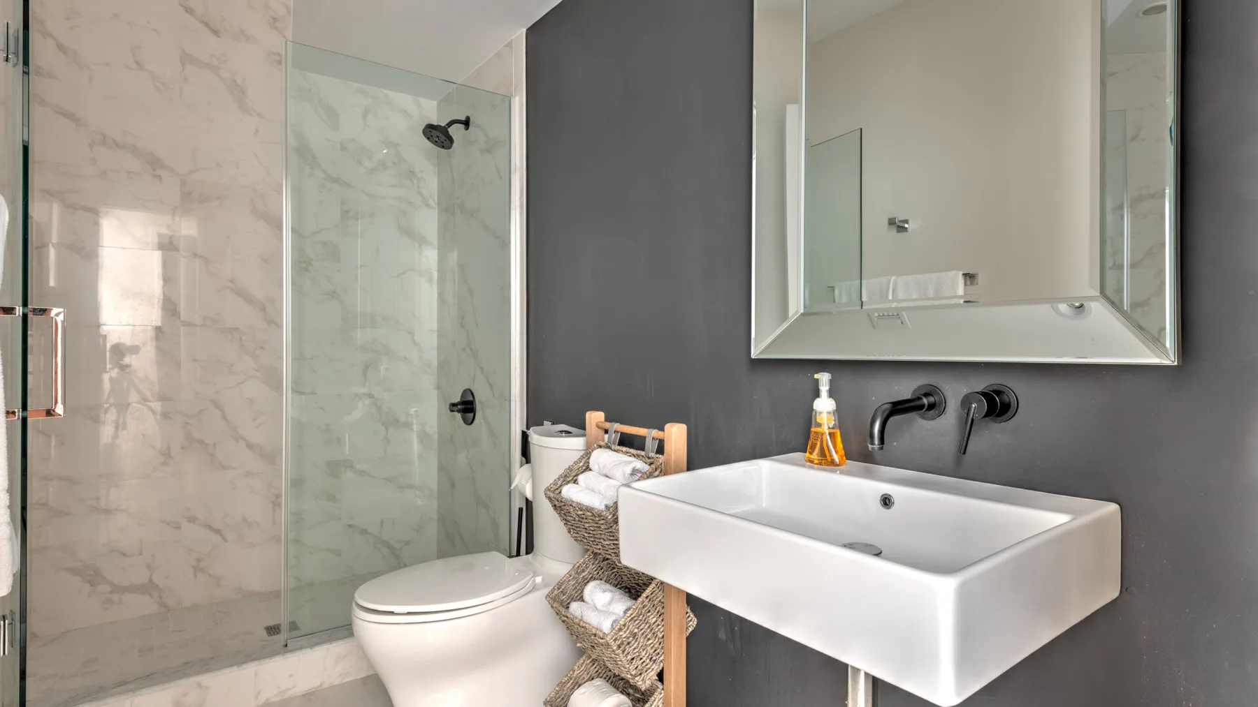 Un baño moderno con ducha de vidrio, inodoro y lavabo montado en la pared.
