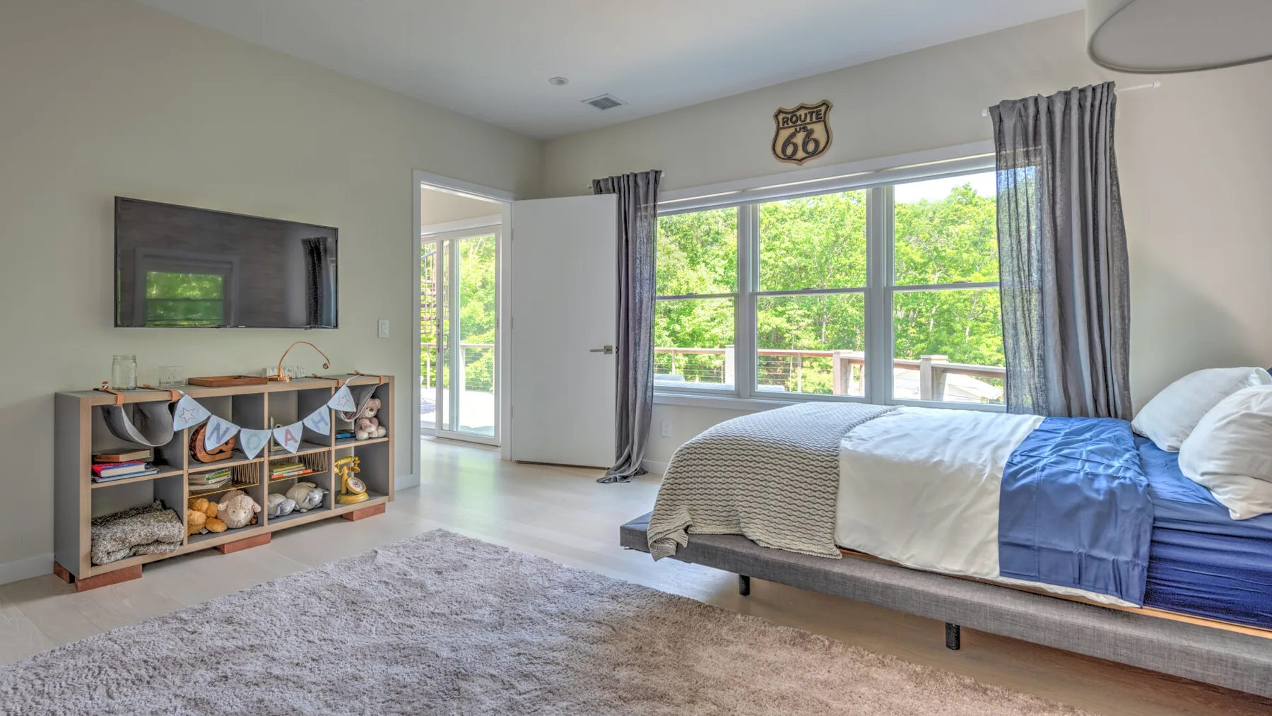 Un dormitorio con una cama, ventanas grandes y un mueble bajo de almacenaje.