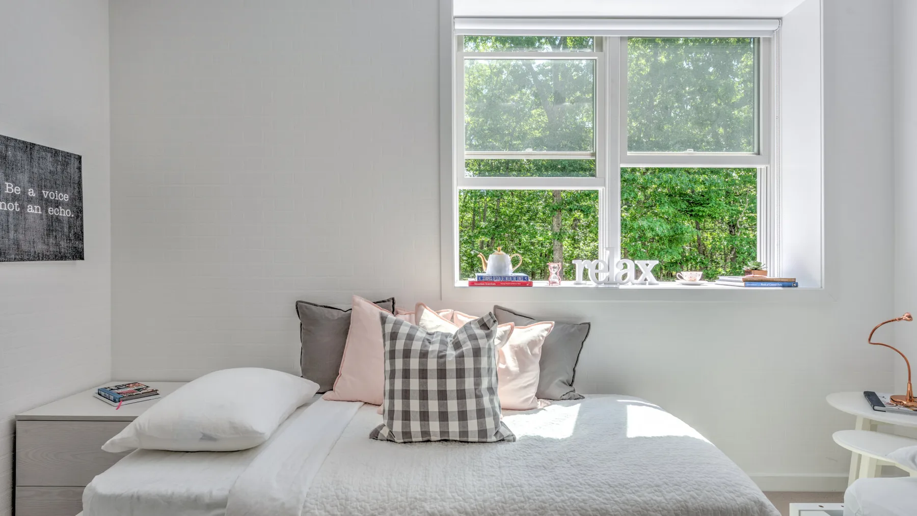 Un dormitorio con una cama bien tendida bajo una ventana grande.