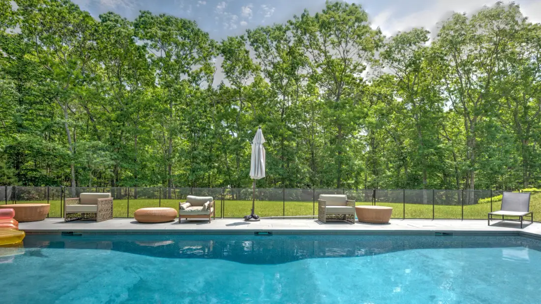 Una piscina al aire libre junto a un jardín arbolado, con tumbonas y sombrillas.