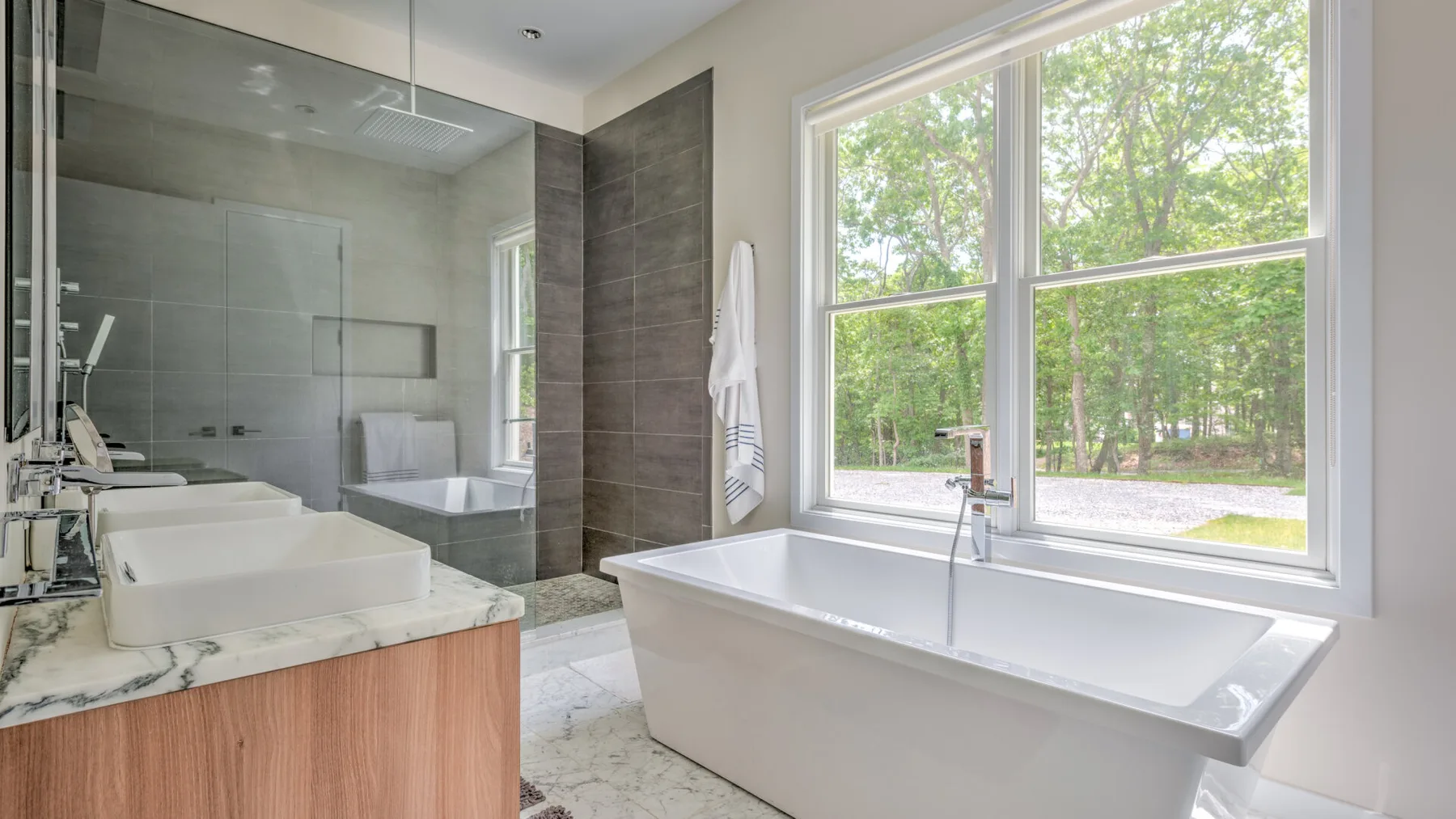 Un baño con una bañera junto a una gran ventana con vista a los árboles.