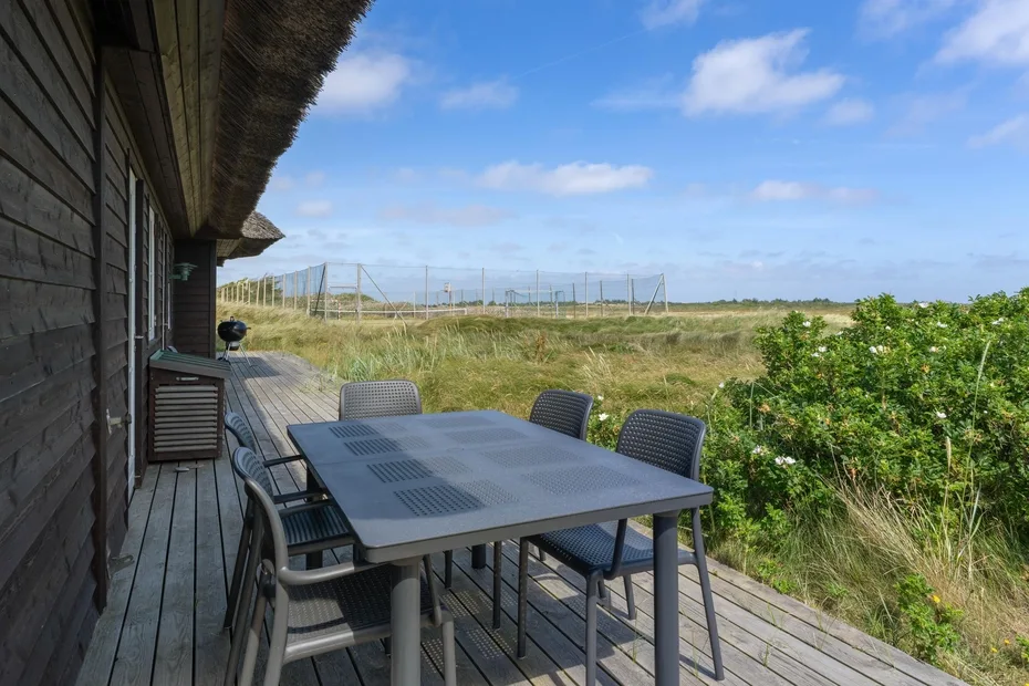 Una zona de comedor al aire libre con mesa y asientos junto a un campo de hierba.
