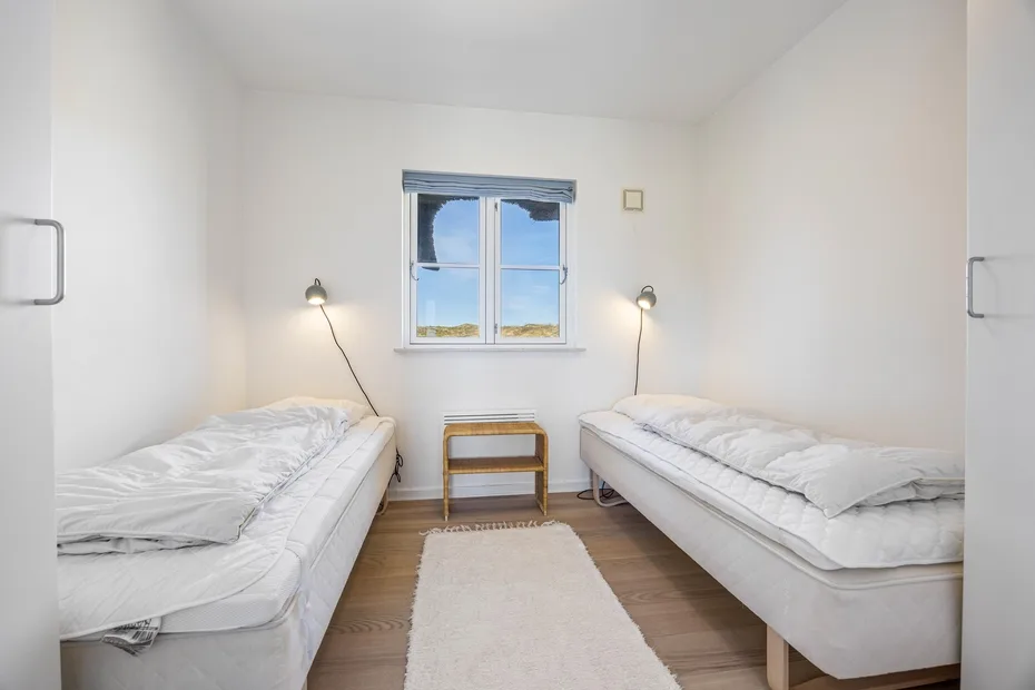 Un dormitorio luminoso con dos camas frente a una ventana y una mesa pequeña.