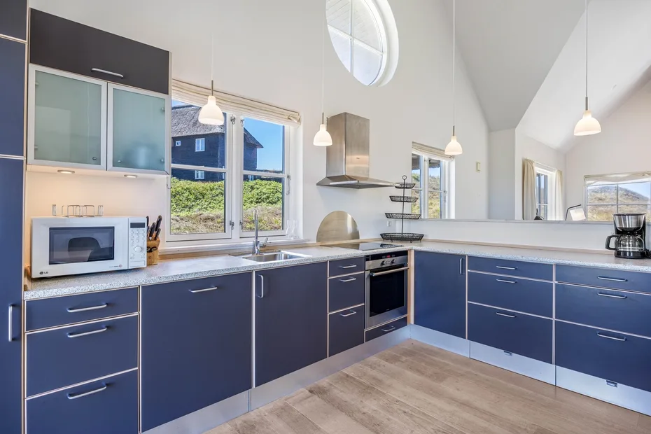 Una cocina amplia con gabinetes azules, una encimera central y ventanas grandes.