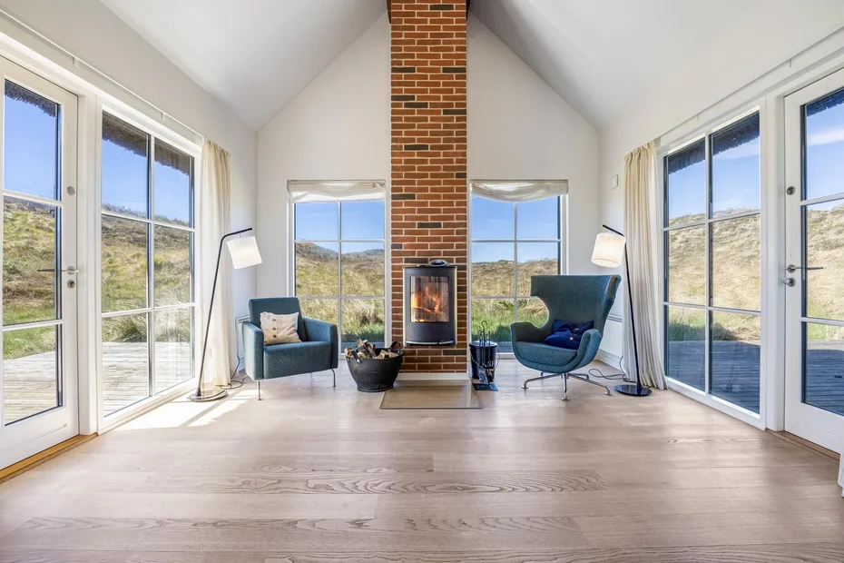 Una sala luminosa tiene una chimenea central de ladrillo y asientos junto a grandes ventanales.