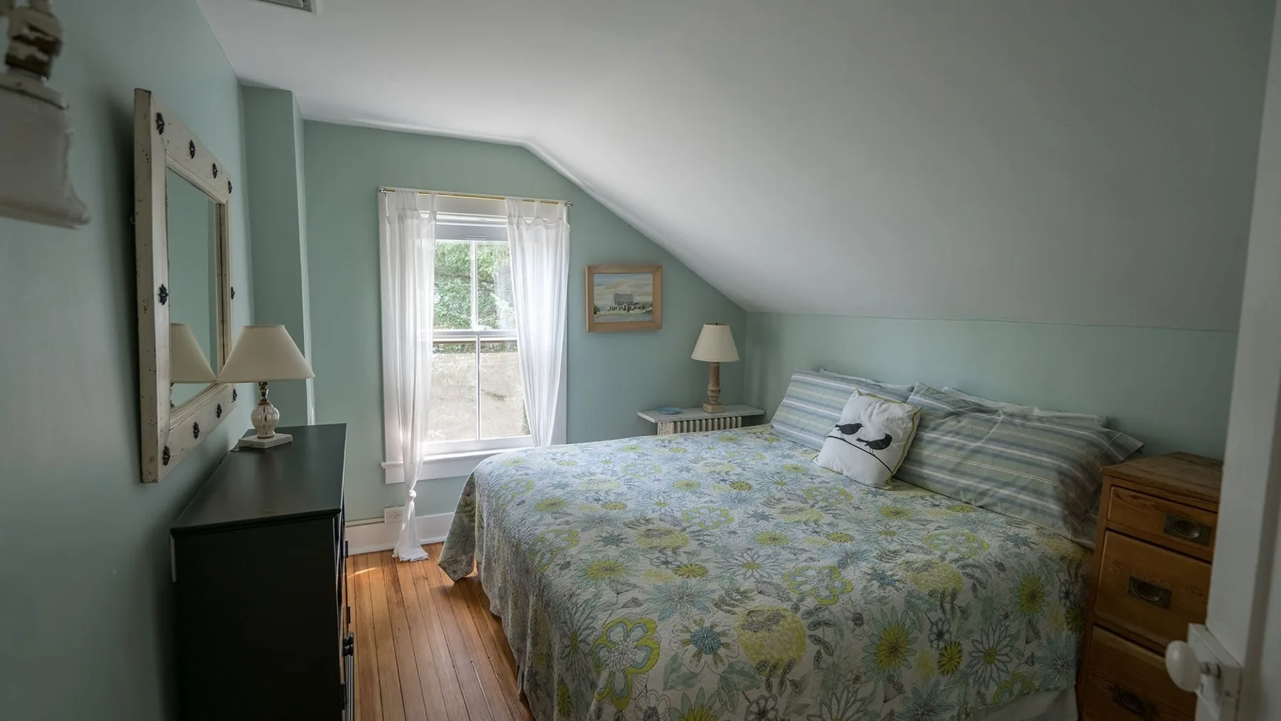 Un dormitorio con una colcha estampada, una ventana y paredes inclinadas.