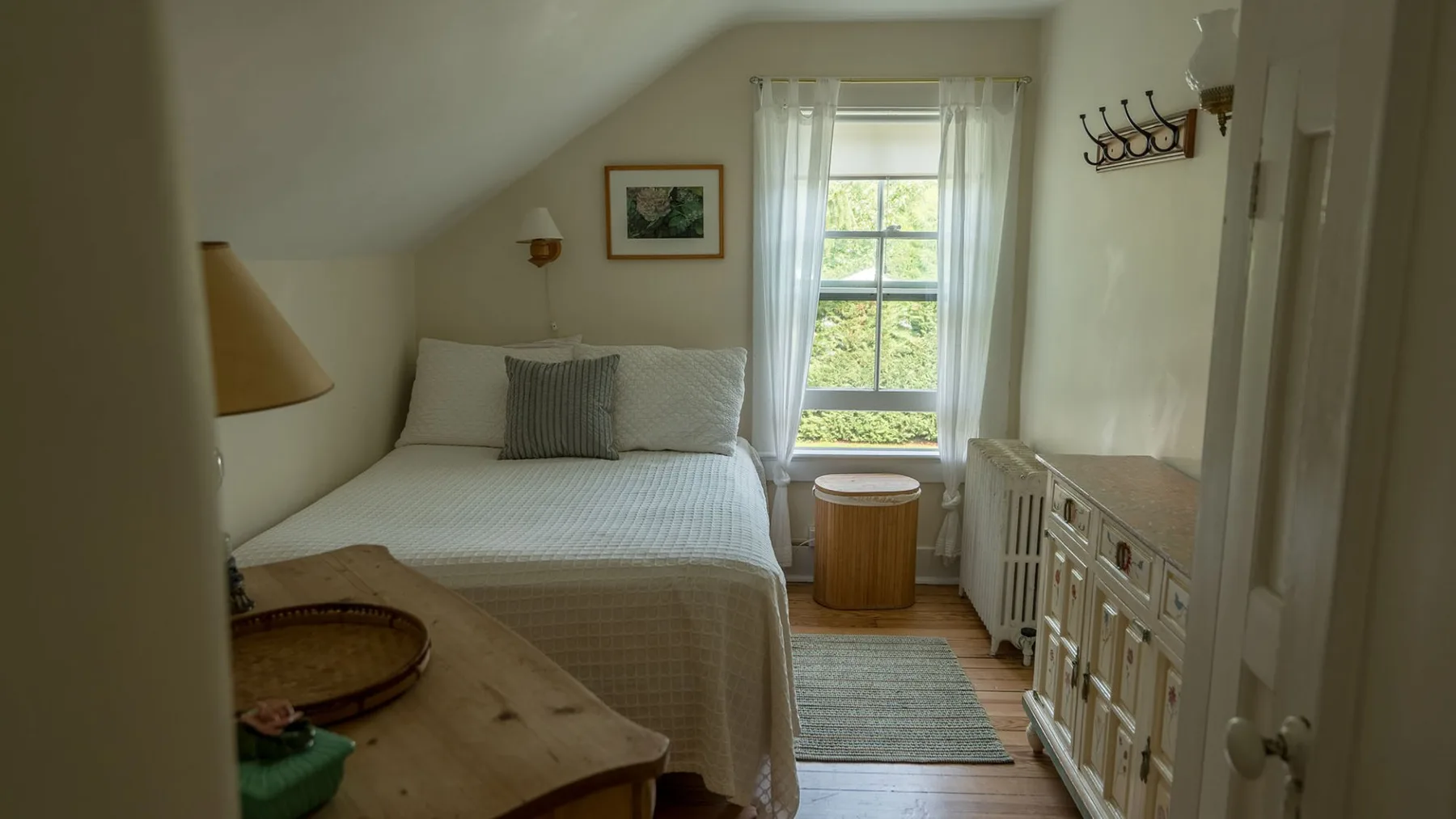 Un dormitorio luminoso con una cama junto a una ventana y una cómoda de madera.
