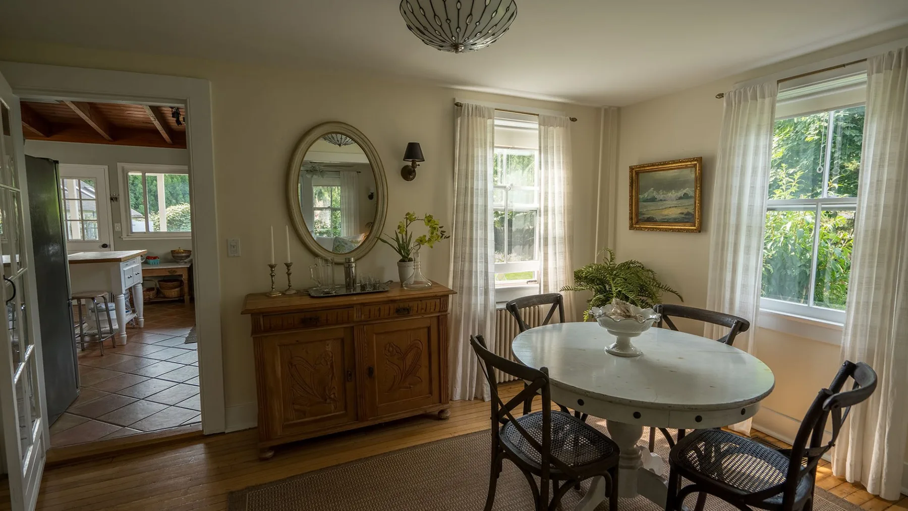Un comedor con una mesa redonda y un aparador de madera junto a ventanas luminosas.