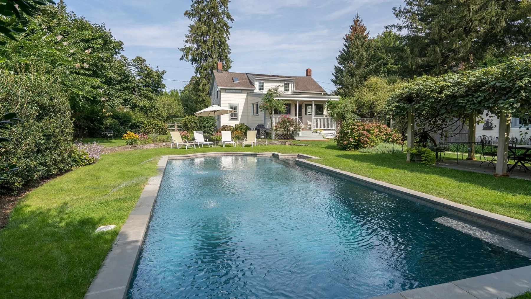 Una piscina está en un césped frente a una casa blanca.
