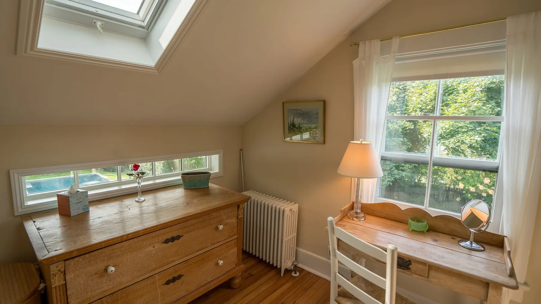 Una luminosa habitación abuhardillada con un escritorio bajo una ventana grande y una claraboya.