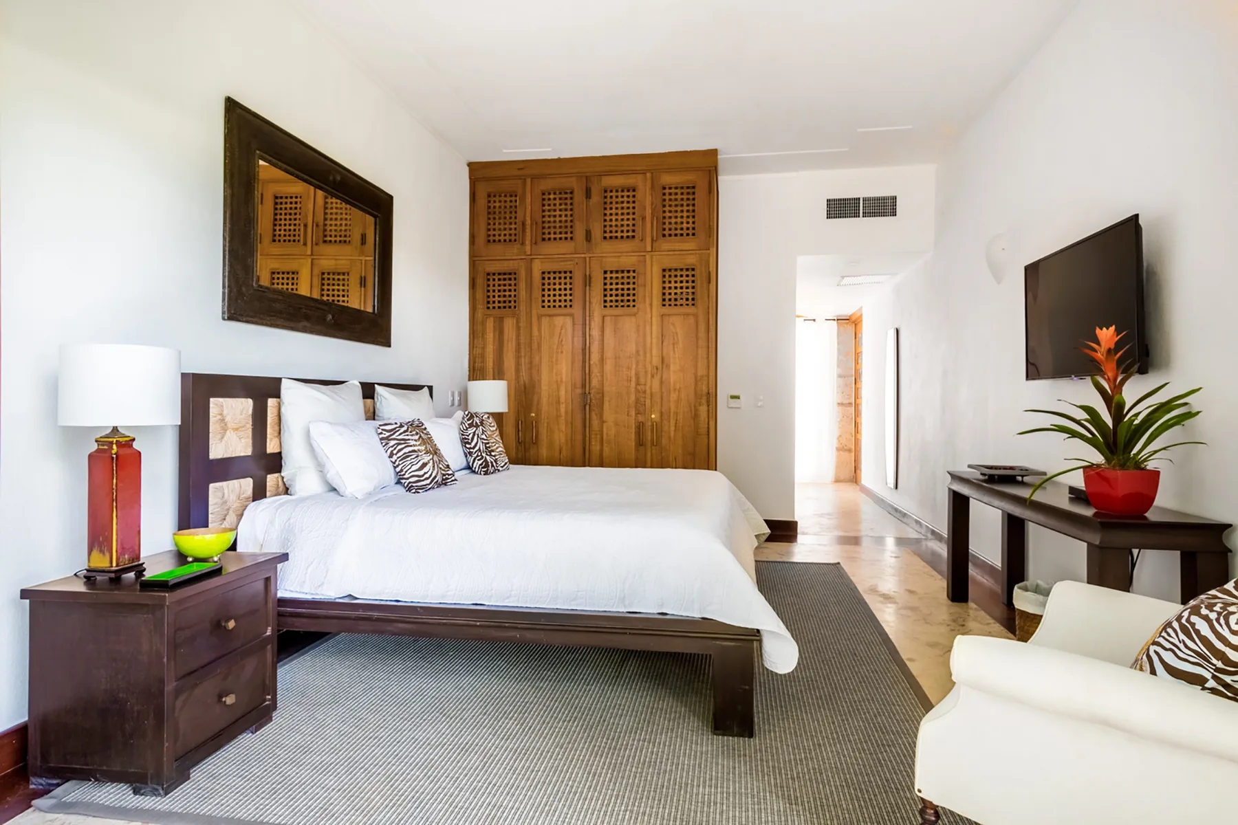 Un dormitorio con una cama grande, un armario de madera y un televisor montado en la pared.
