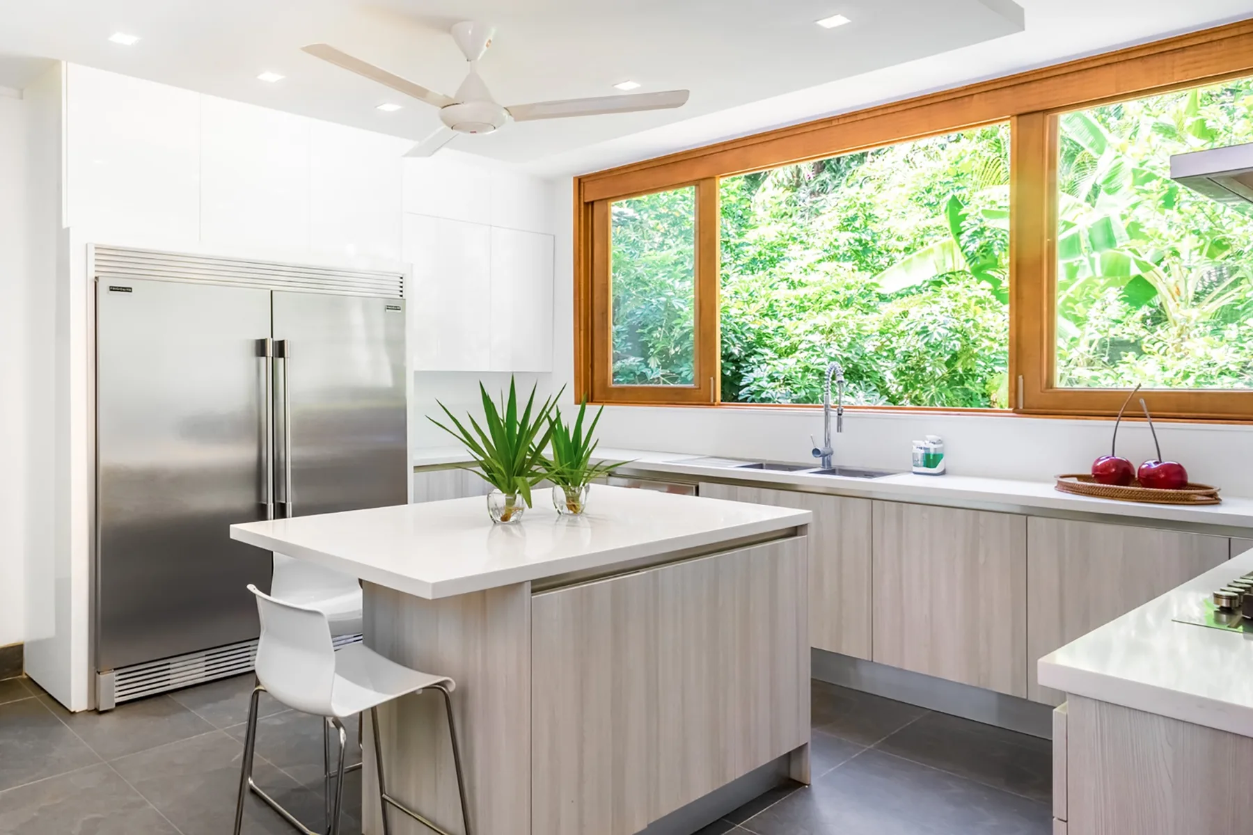 Una cocina moderna y luminosa con una isla central y amplias ventanas con vista a la vegetación.
