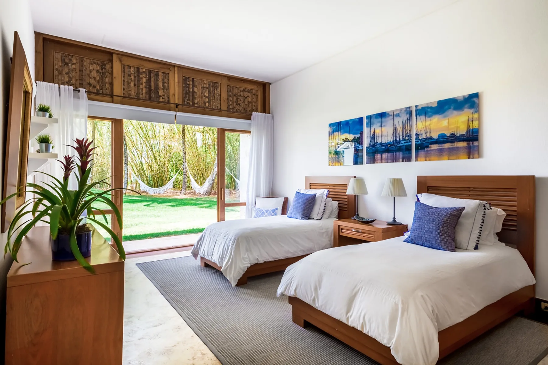 Dormitorio con dos camas, mesitas de noche y puertas de vidrio que dan a un jardín.