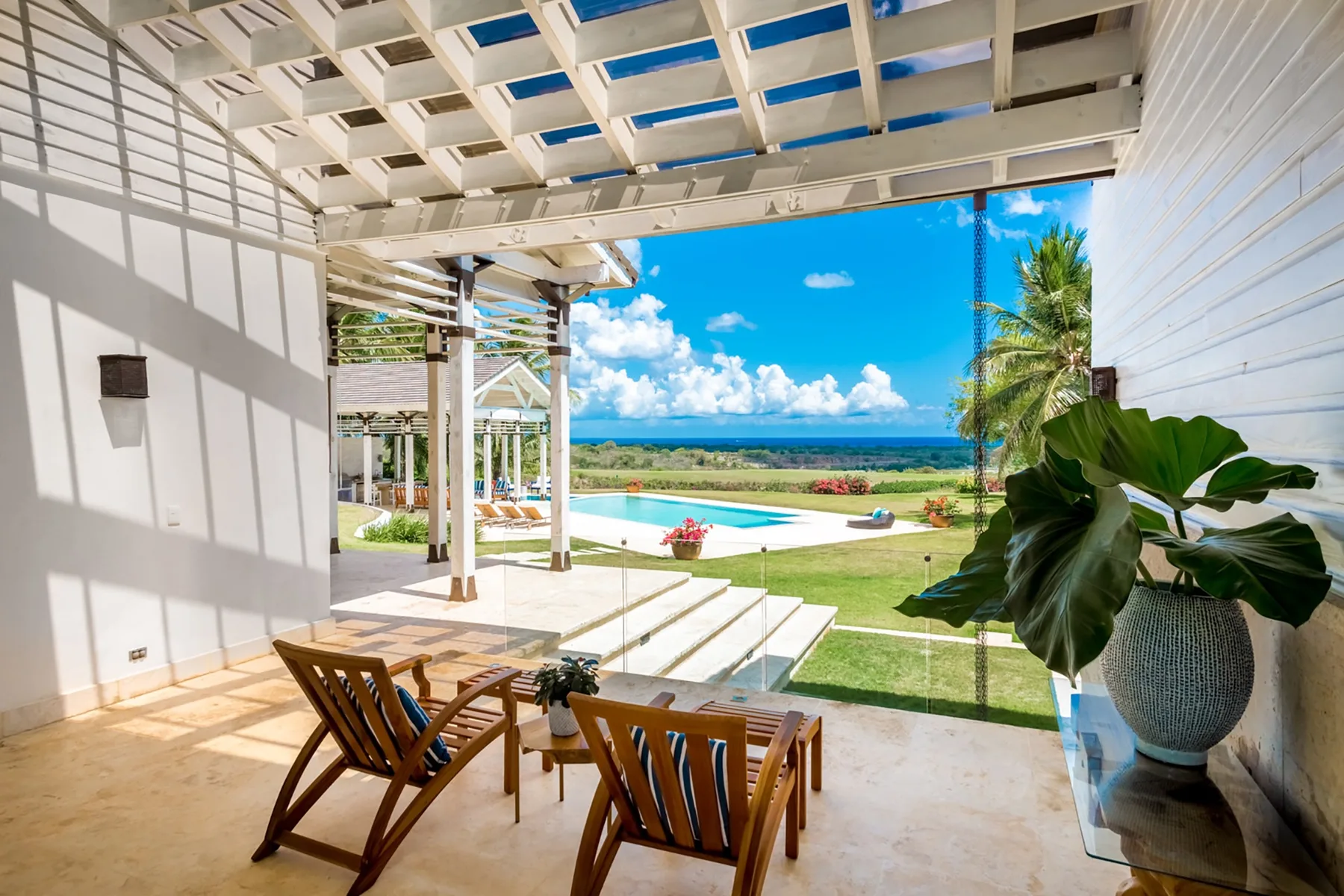A covered patio with seating overlooks a swimming pool and ocean.