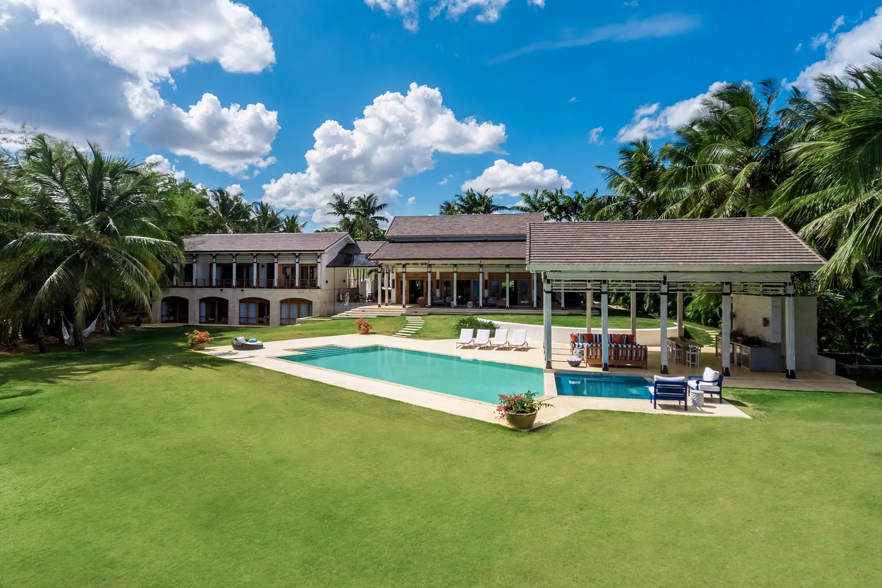 Tropical villa and swimming pool surrounded by a broad green lawn.