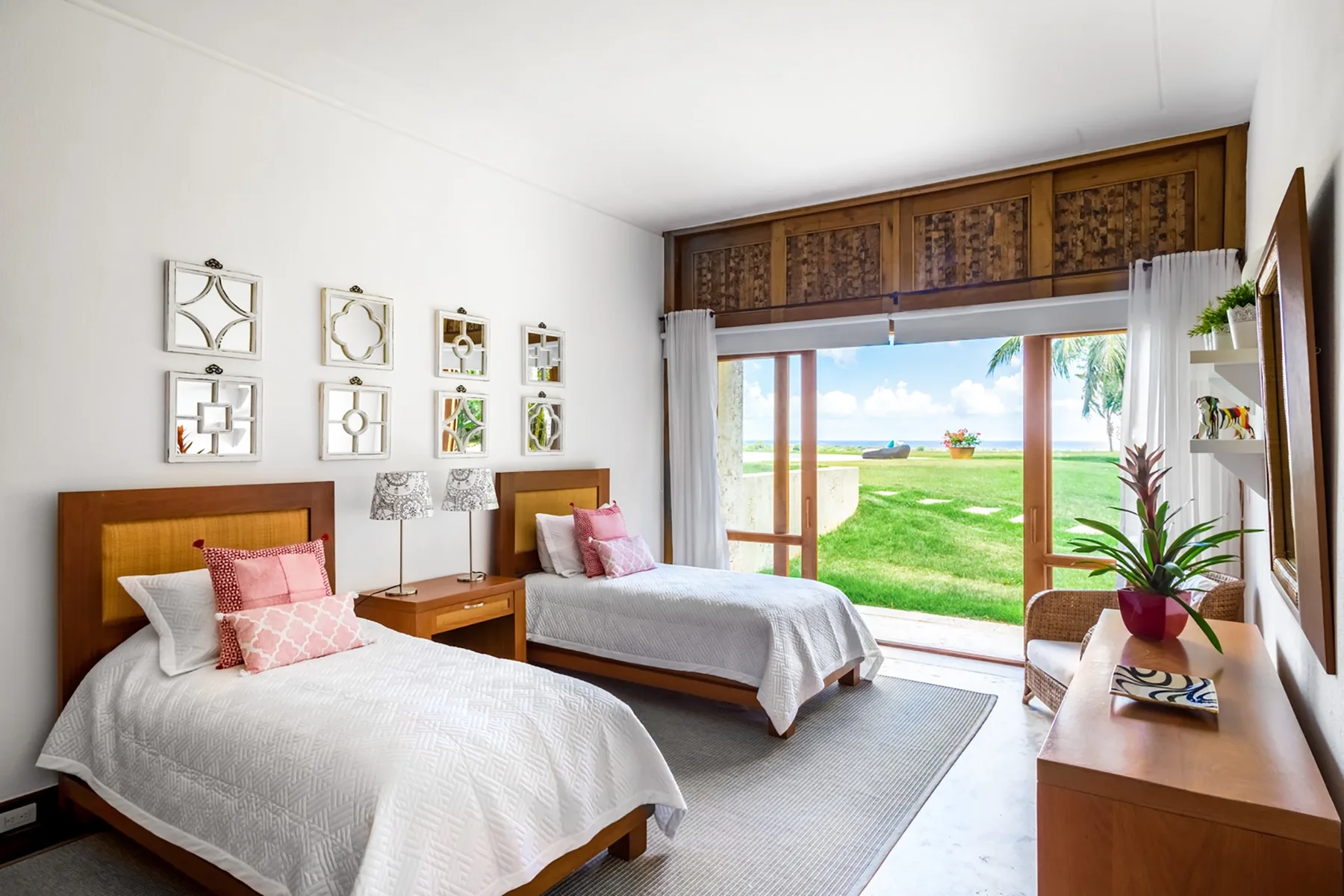 Un dormitorio luminoso con dos camas, cuadros en la pared y vista al césped.