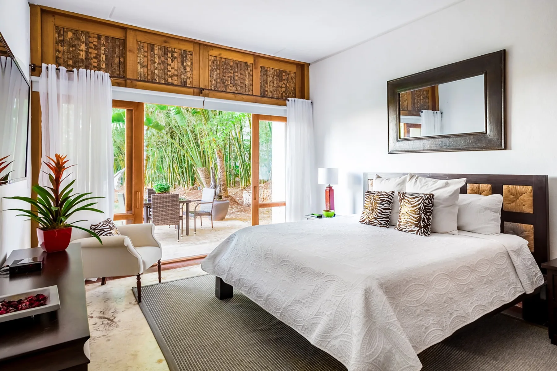 Un dormitorio con una cama grande junto a puertas de vidrio que dan a una zona exterior frondosa.