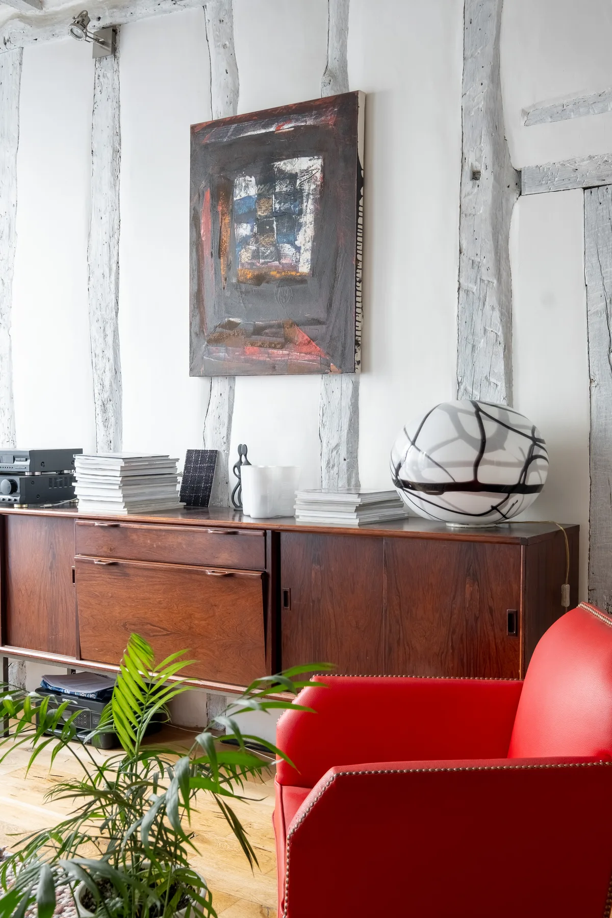 A bright living area with a wooden sideboard, red seating, and a potted palm.