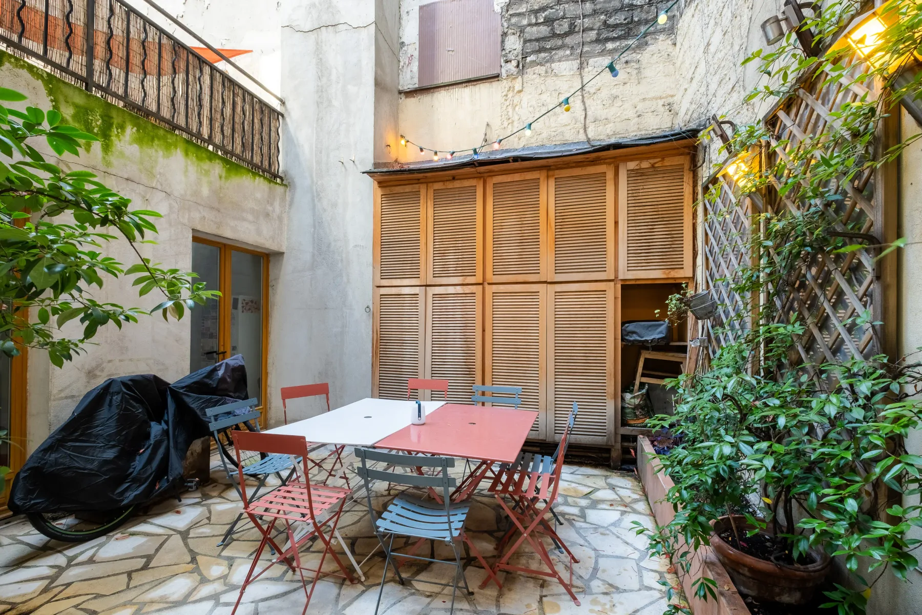 A courtyard dining area with a table and chairs beside wooden shutters.