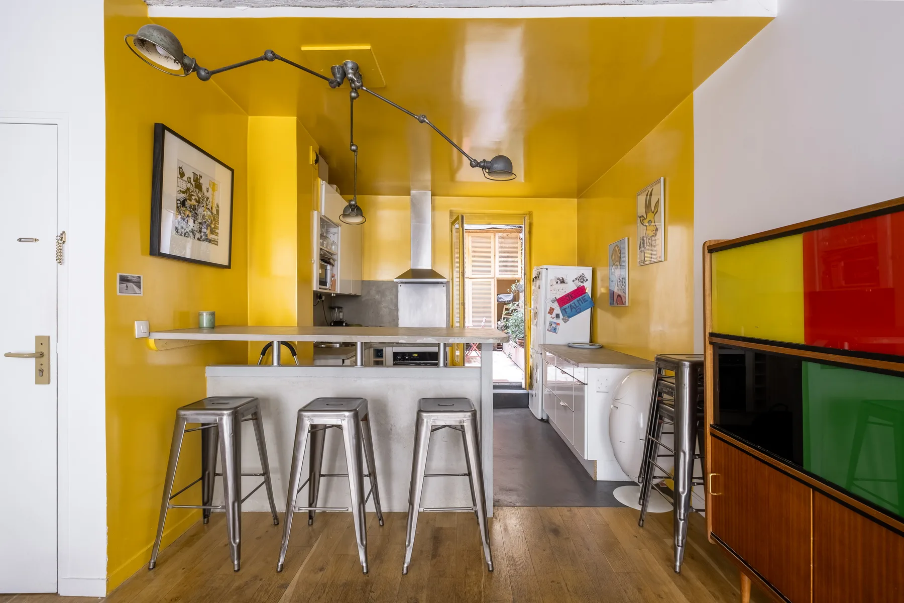 A bright yellow kitchen with a counter, stools, and cooking appliances.