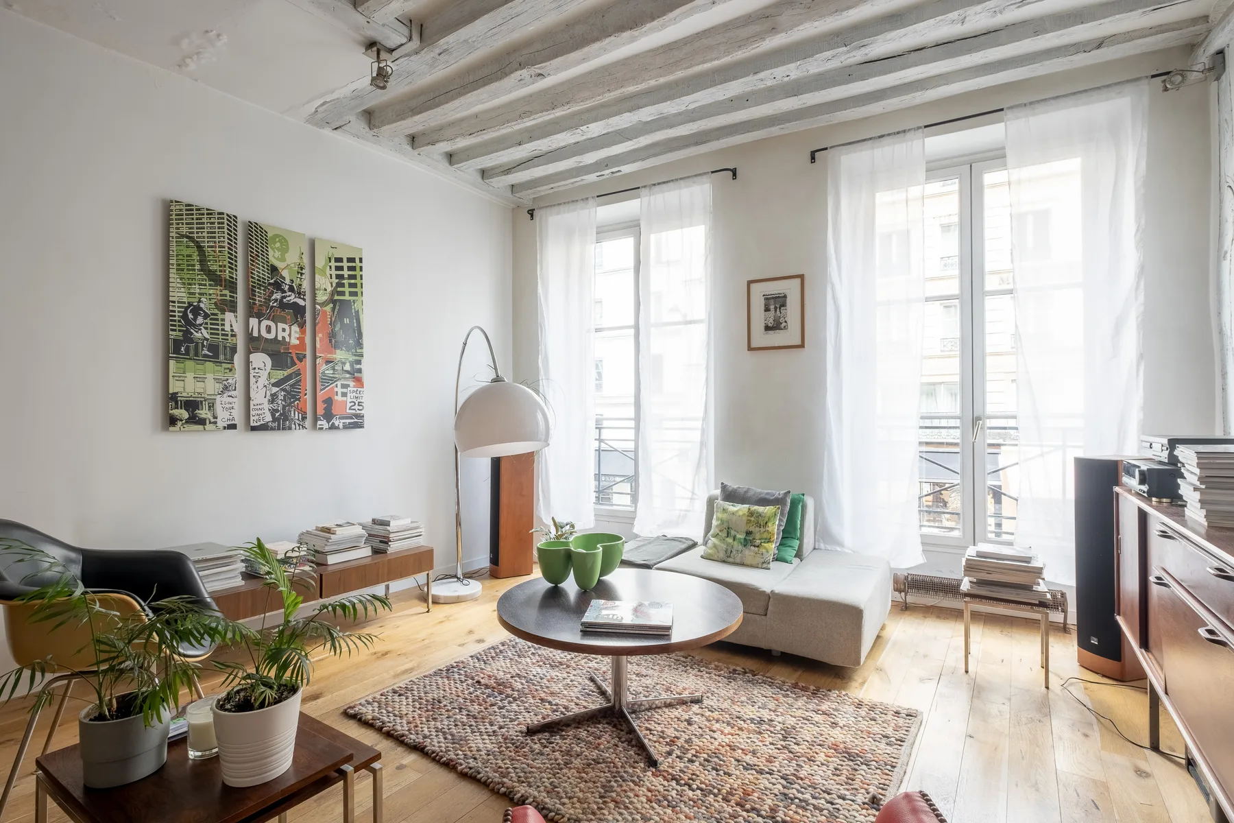 A bright living room with seating, a coffee table, plants, and tall windows.