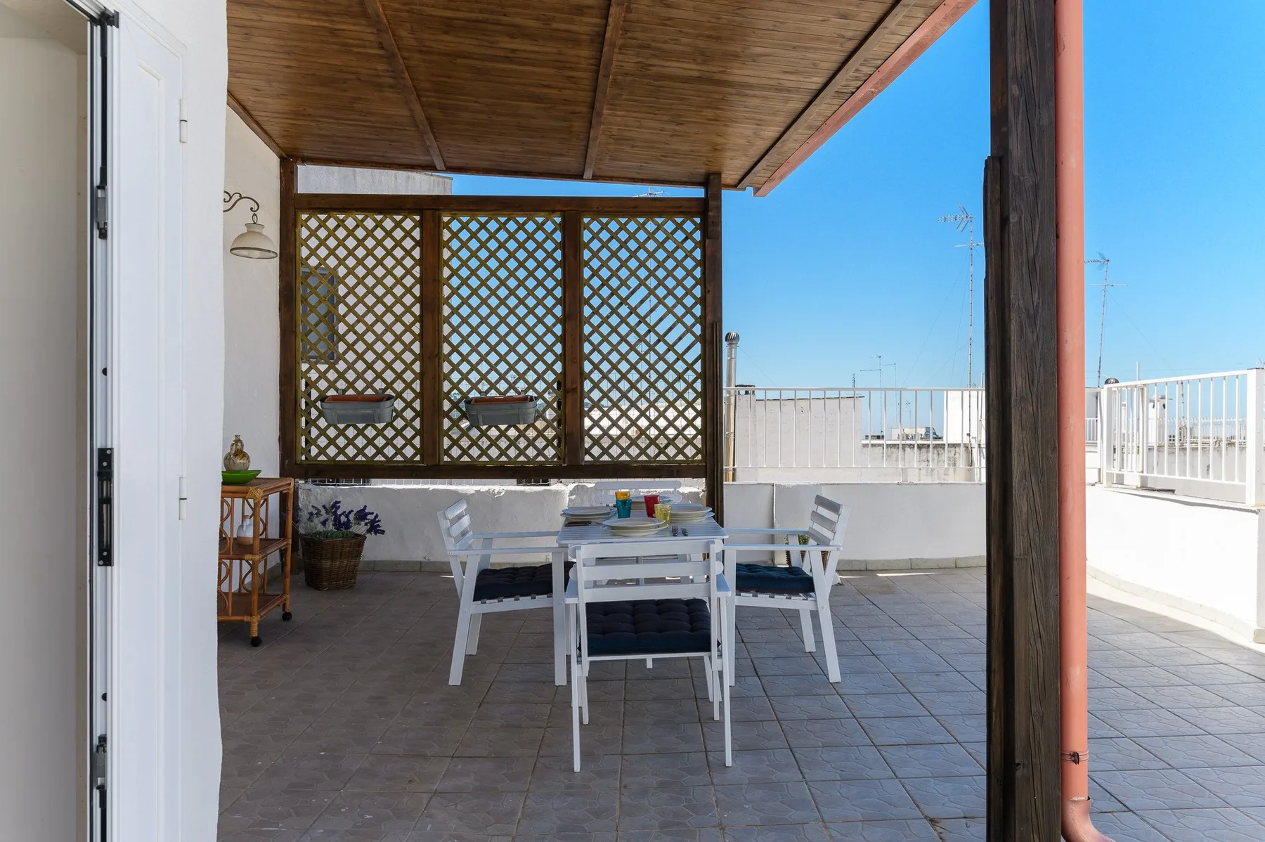 A covered outdoor dining area with white seating and a lattice screen.