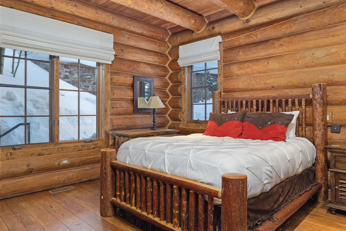 A bedroom with a wooden bed and snowy views through the windows.
