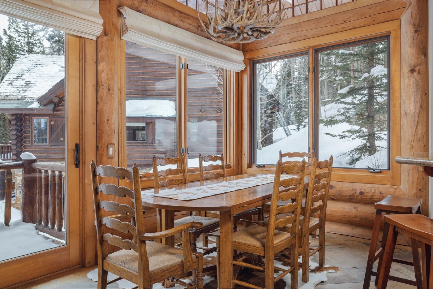 A wooden dining area with a long table and large windows overlooking a snowy landscape.