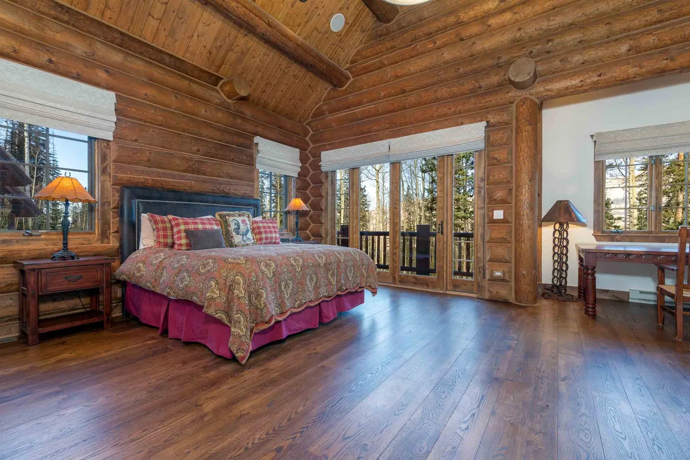 A log-cabin bedroom with a large bed and windows overlooking trees.