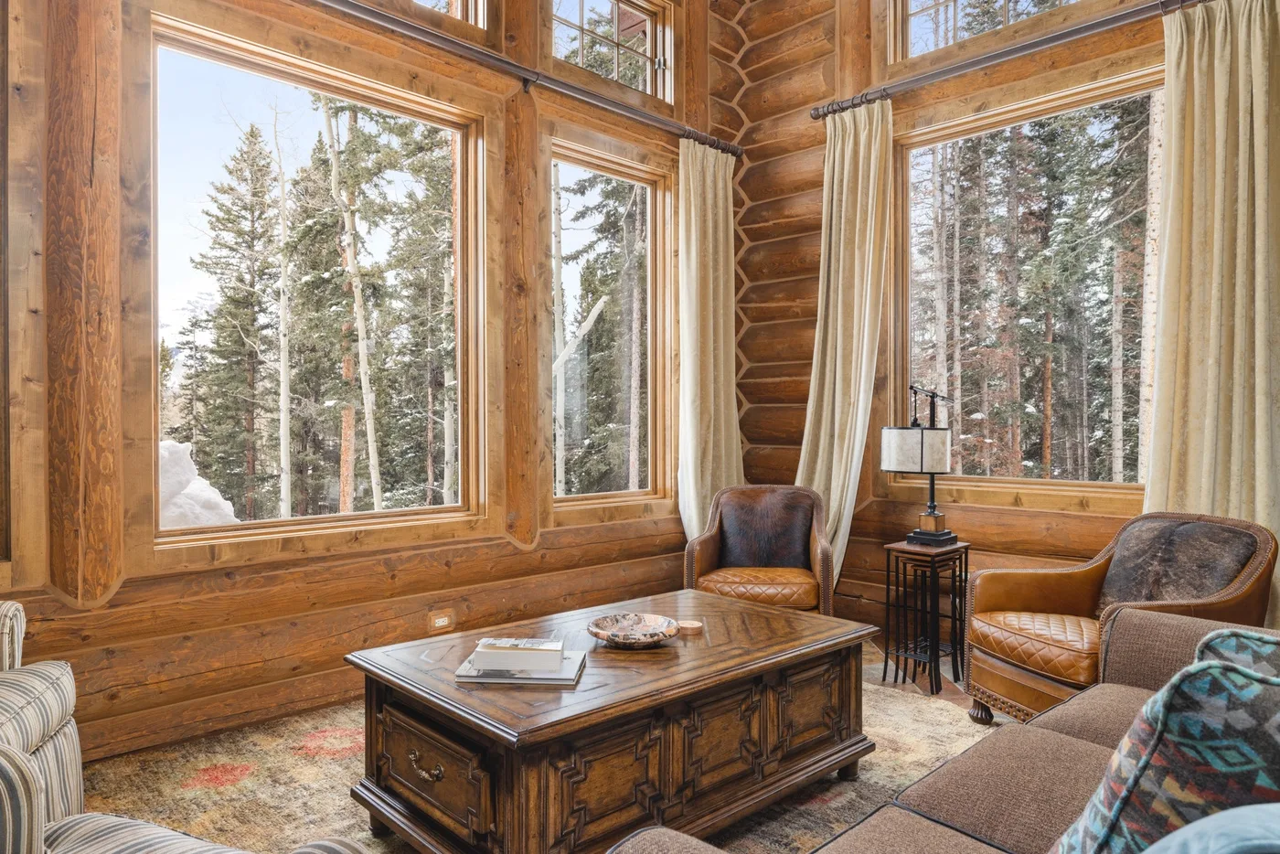 A wood-paneled living room with large windows, seating, and a coffee table.