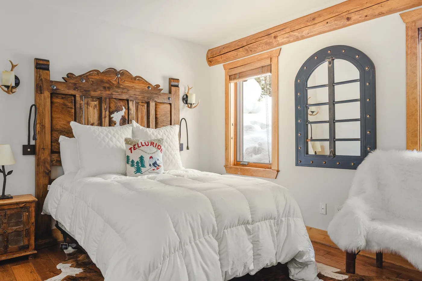 A bedroom with a white bed, rustic wooden headboard, and a window.