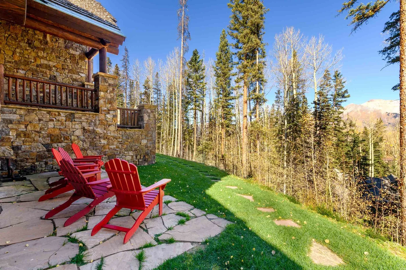 A stone lodge overlooks a grassy yard with red outdoor seating and trees.