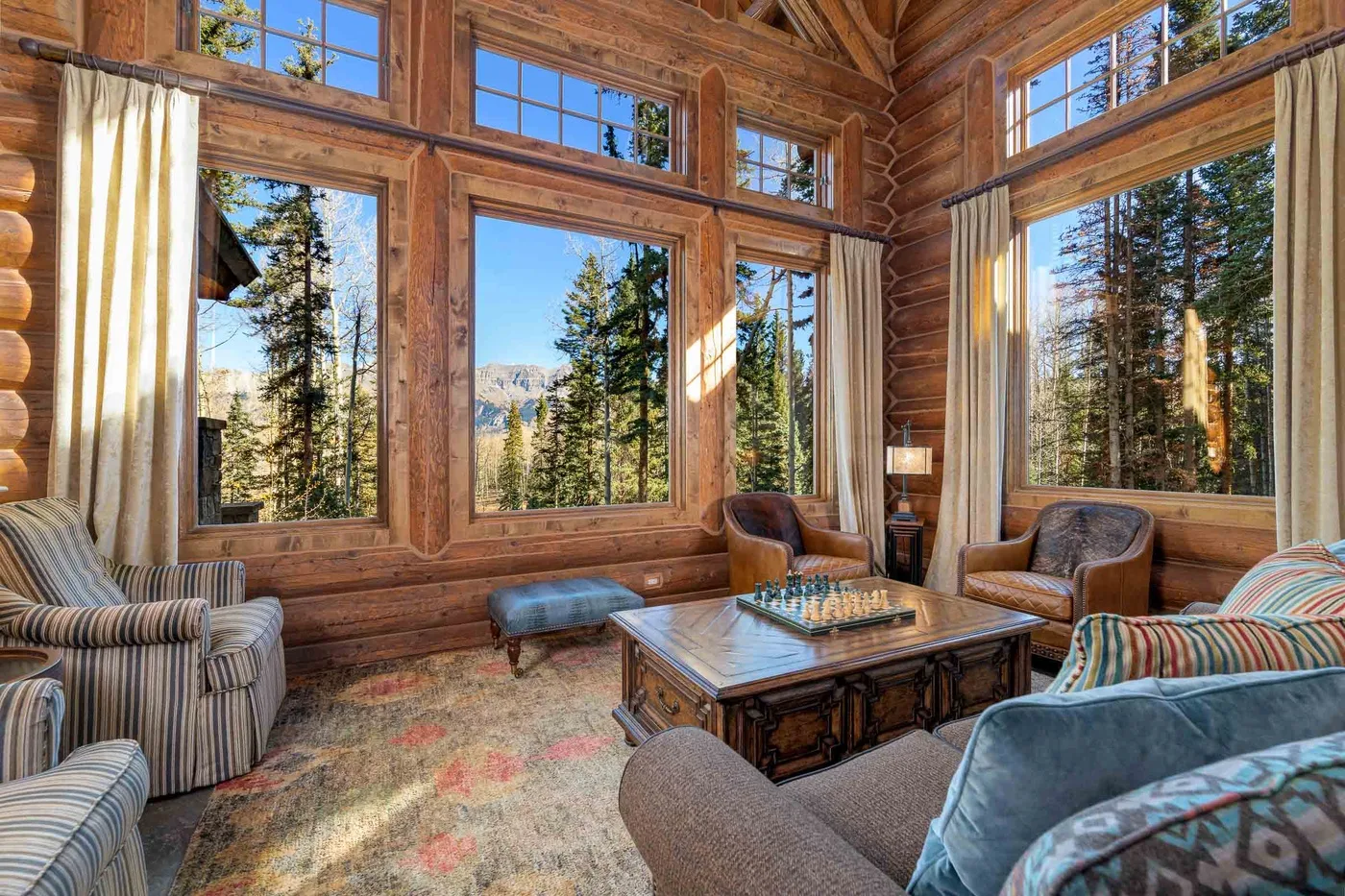 A wood-paneled living room with large windows overlooking a forest.