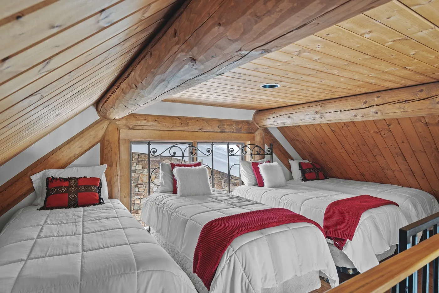 A wood-paneled loft bedroom with several beds dressed in white linens and red runners.