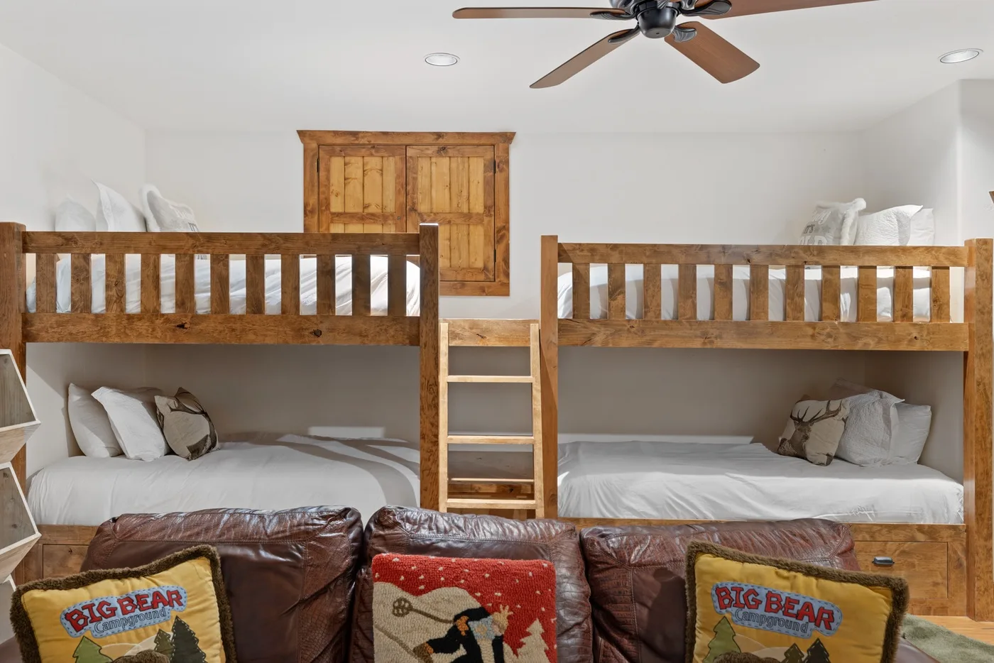 A bedroom with wooden bunk beds, white bedding, and a leather sofa in the foreground.