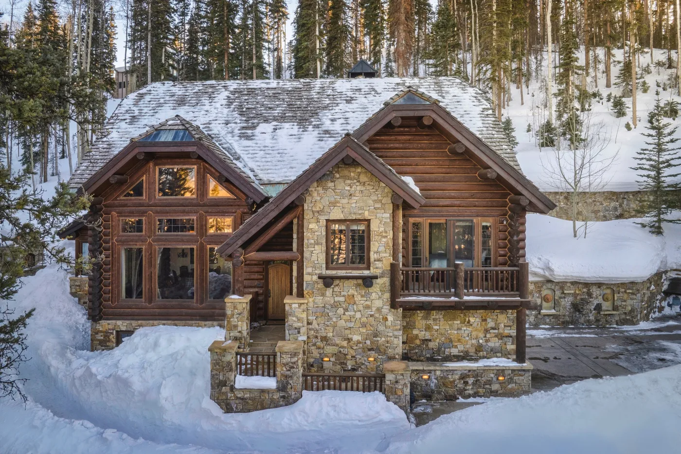 A rustic lodge stands amid snow-covered ground and tall evergreen trees.