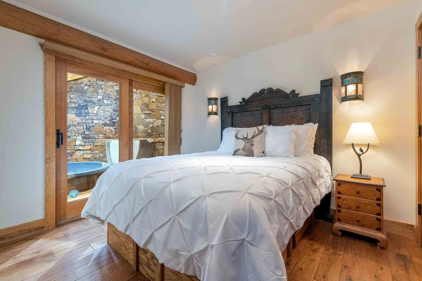 A bedroom with a large bed, wooden headboard, and glass doors opening onto a stone patio.