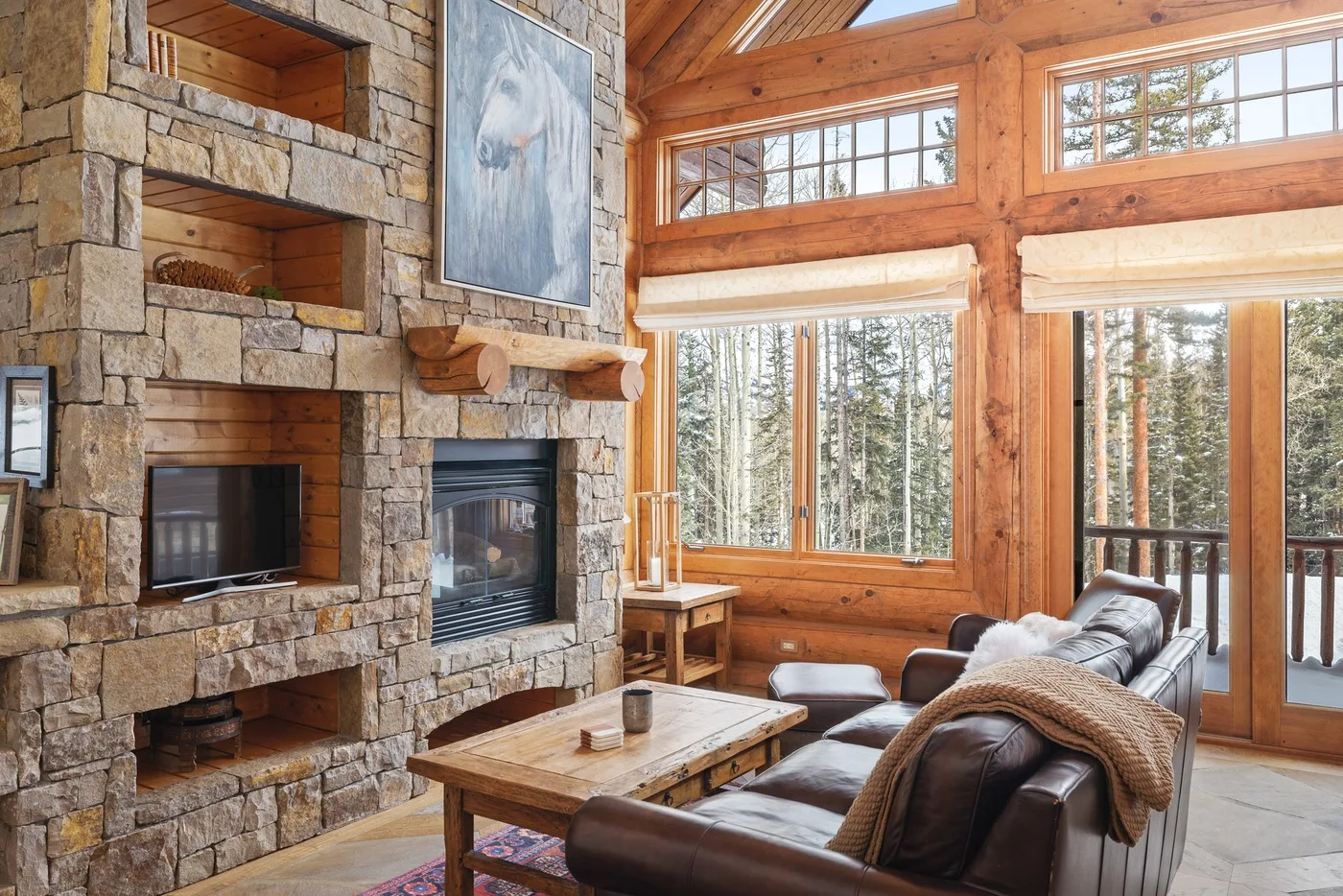 A living room with a stone fireplace, leather seating, and large windows.