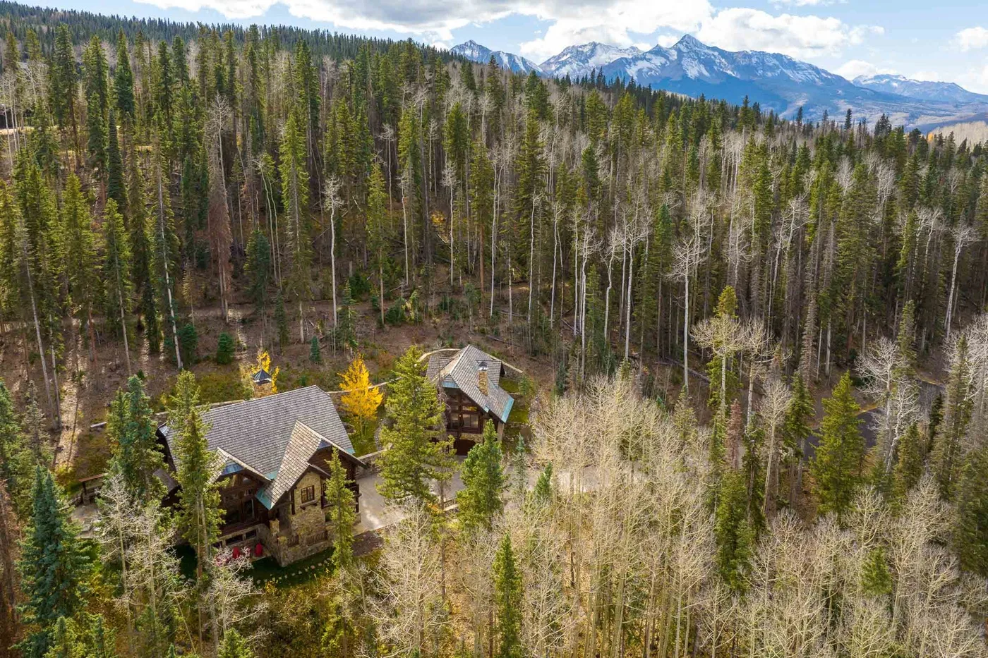 Aerial view of two cabins among trees, with mountains in the distance.