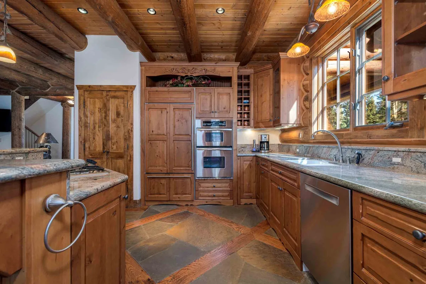 A wood-paneled kitchen with stone countertops, built-in ovens, and windows along the counter.