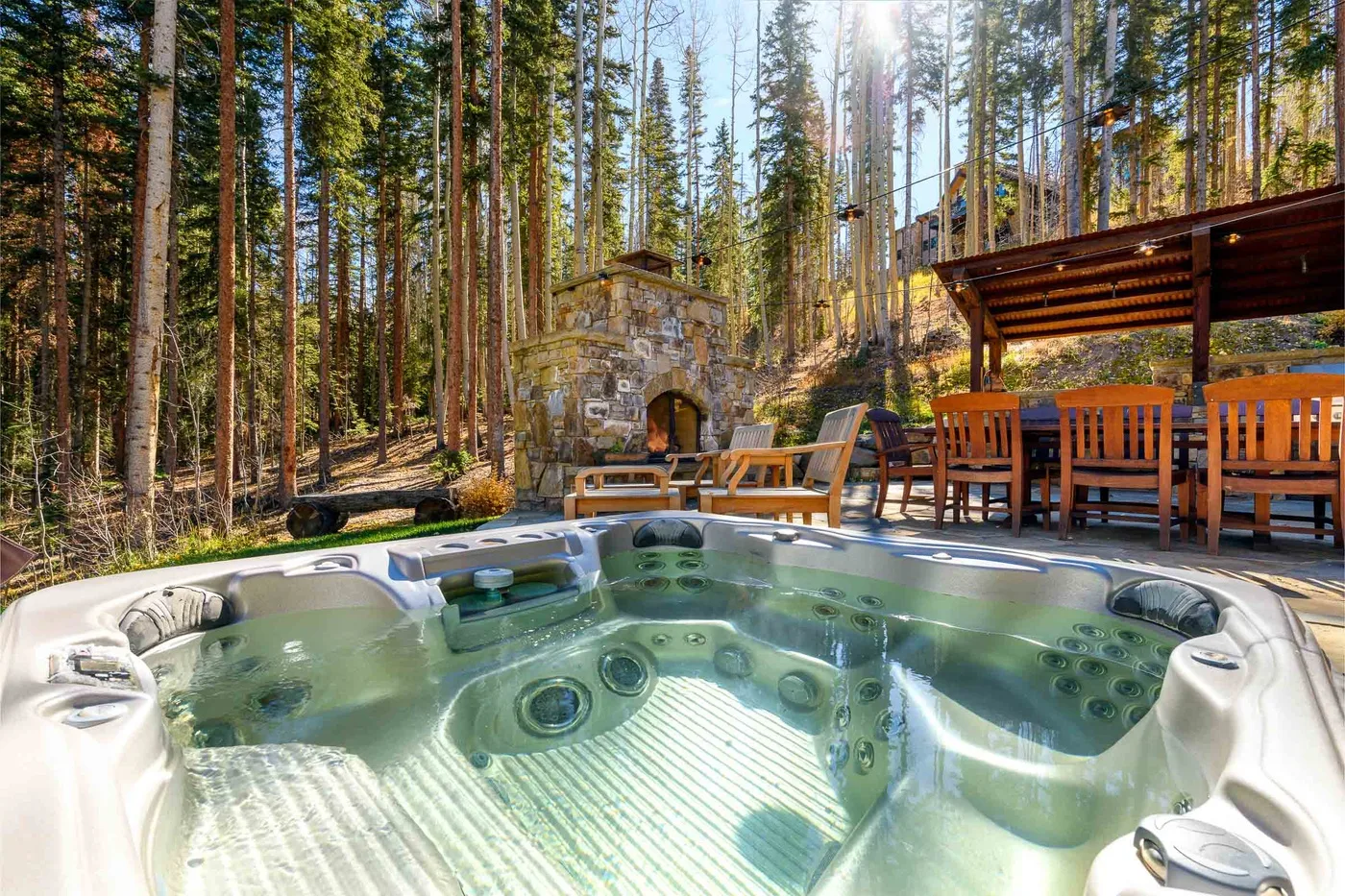 An outdoor hot tub sits beside a wooden dining area in a forest.