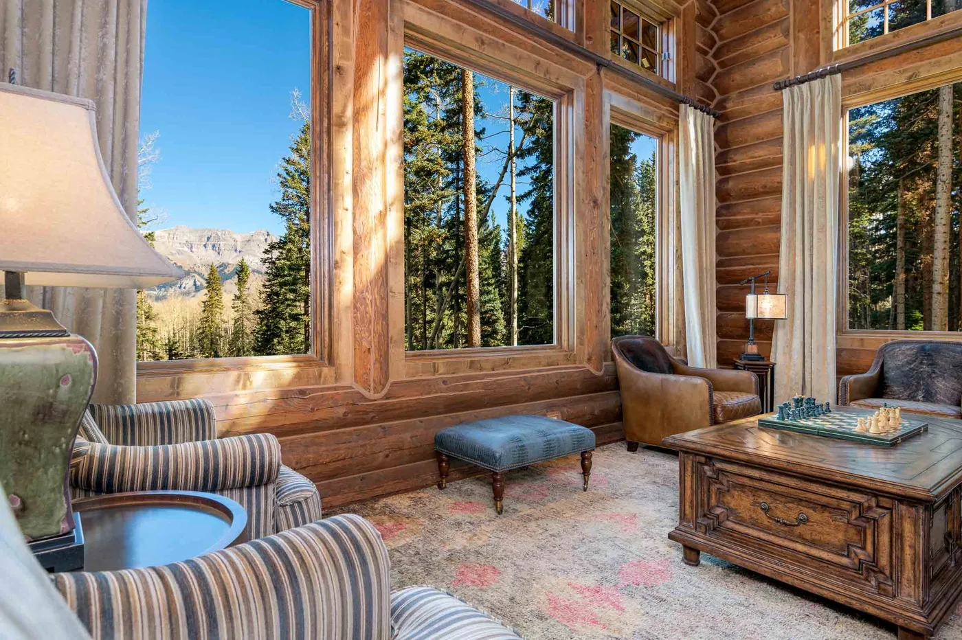 A wood-paneled living room with large windows overlooking trees and mountains.