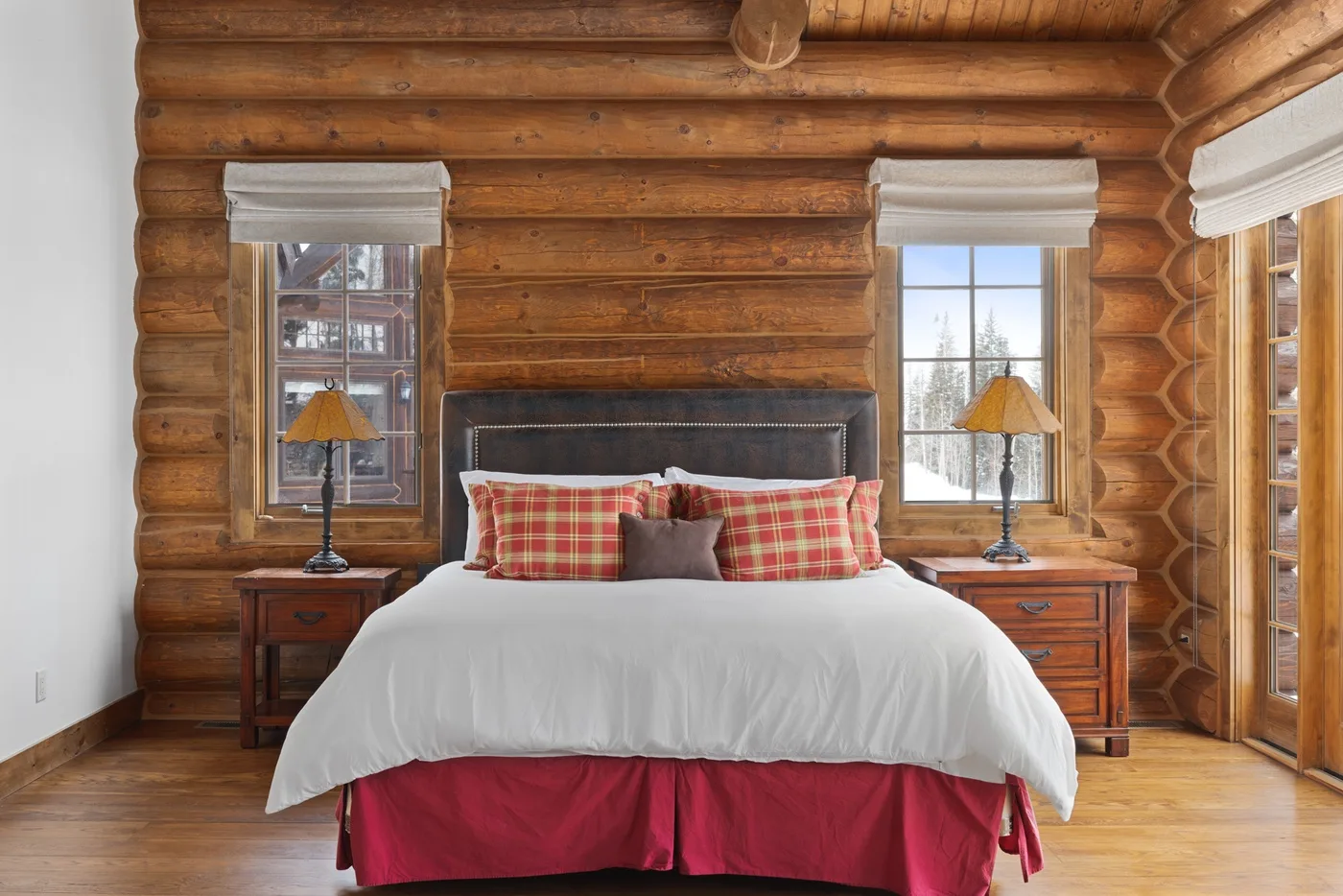 A bedroom with a bed between two windows in a log-walled room.
