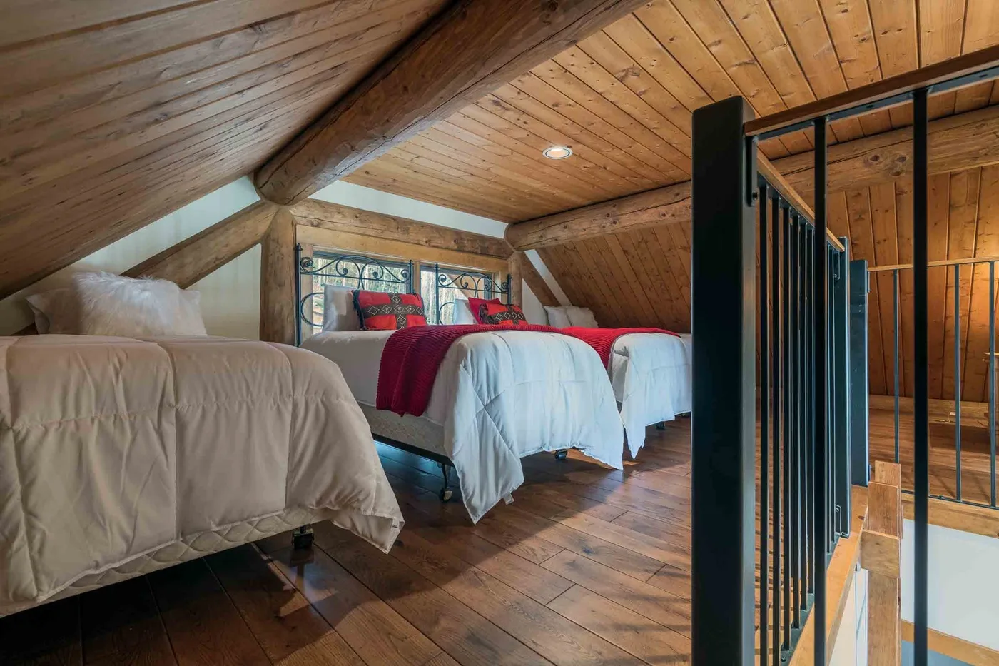 A wood-paneled loft bedroom with beds and a black railing.