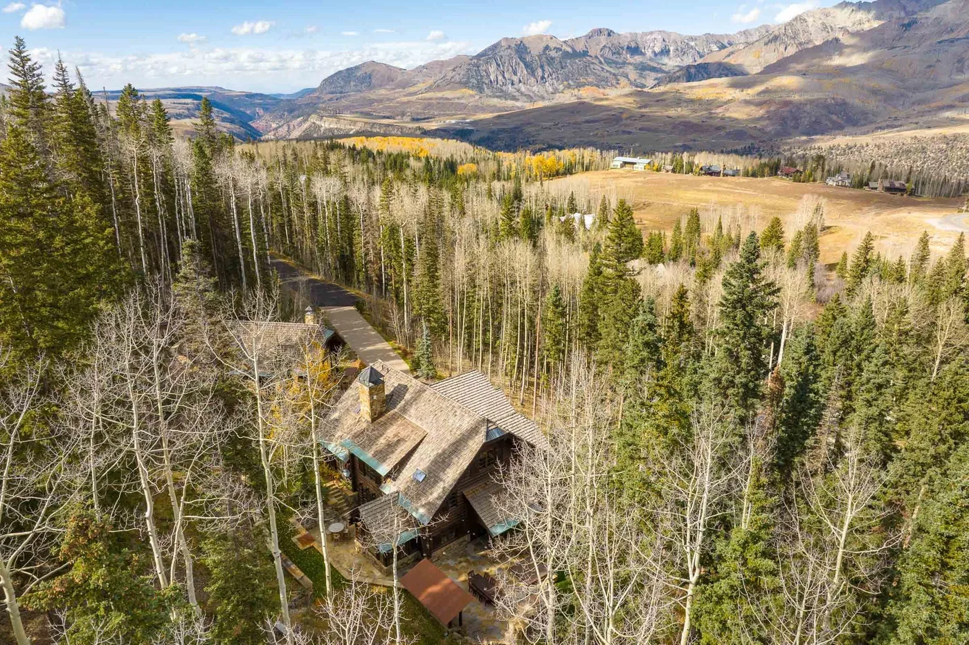 A cabin sits among forest trees, with an open valley and mountains beyond.
