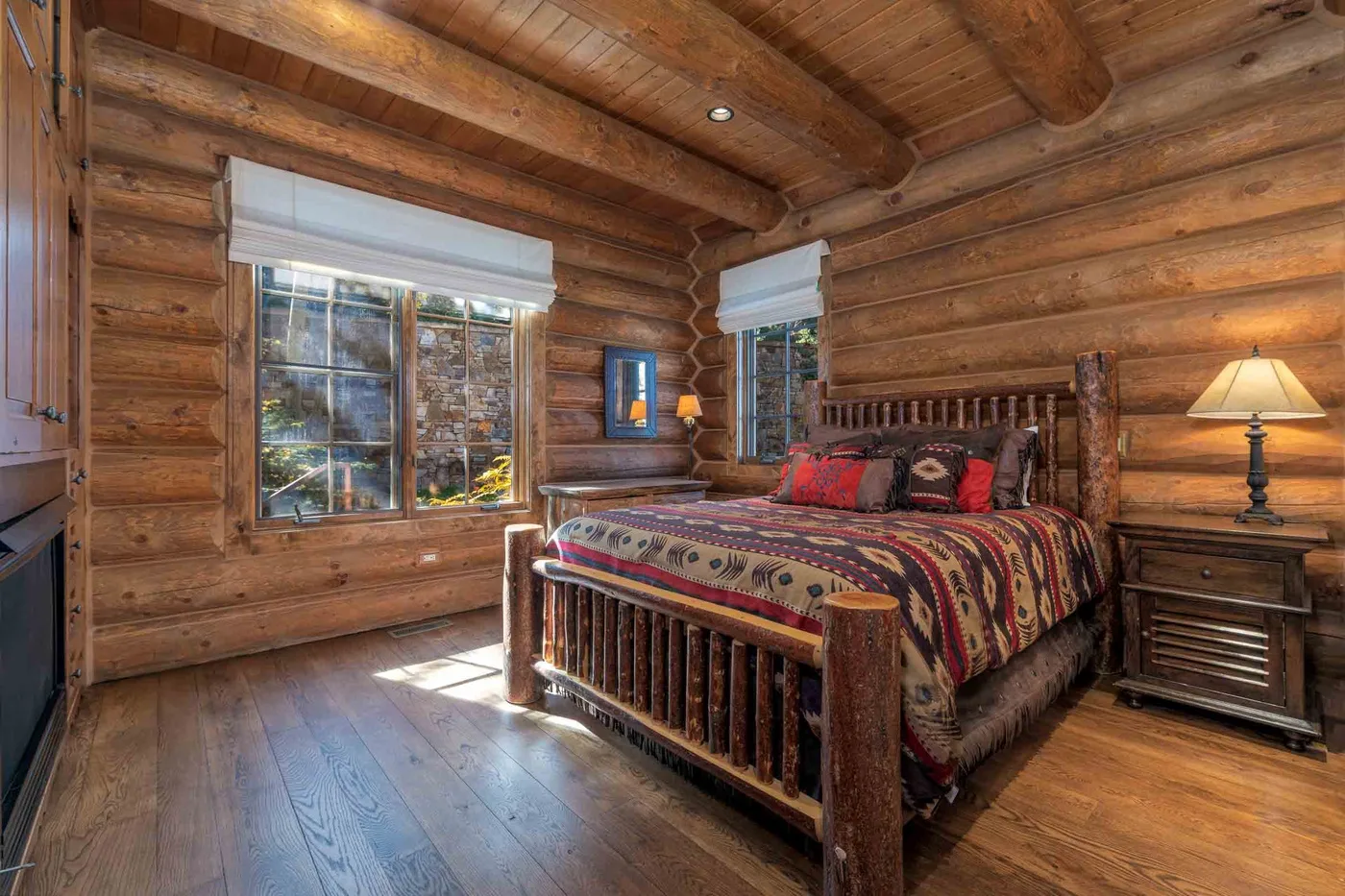 A wooden bedroom with a bed, windows, and a bedside table.