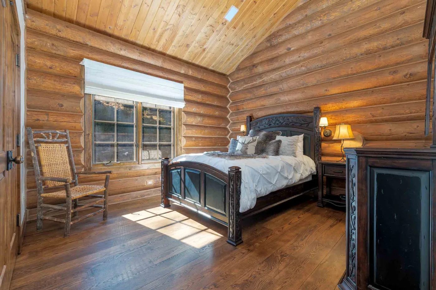 A bedroom with a bed, wooden walls, and a window letting in sunlight.