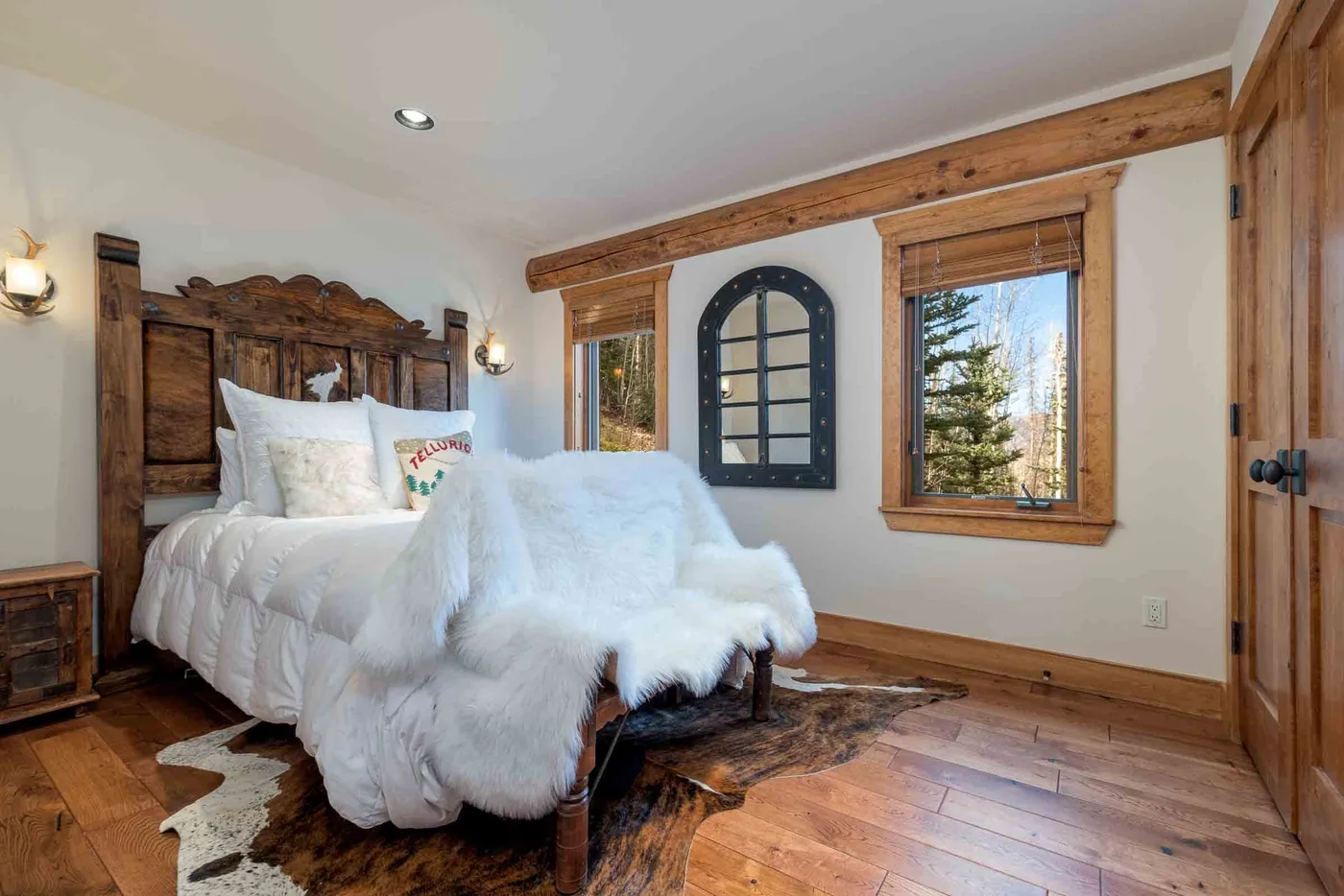 A bedroom with a wooden bed, white bedding, and windows overlooking trees.